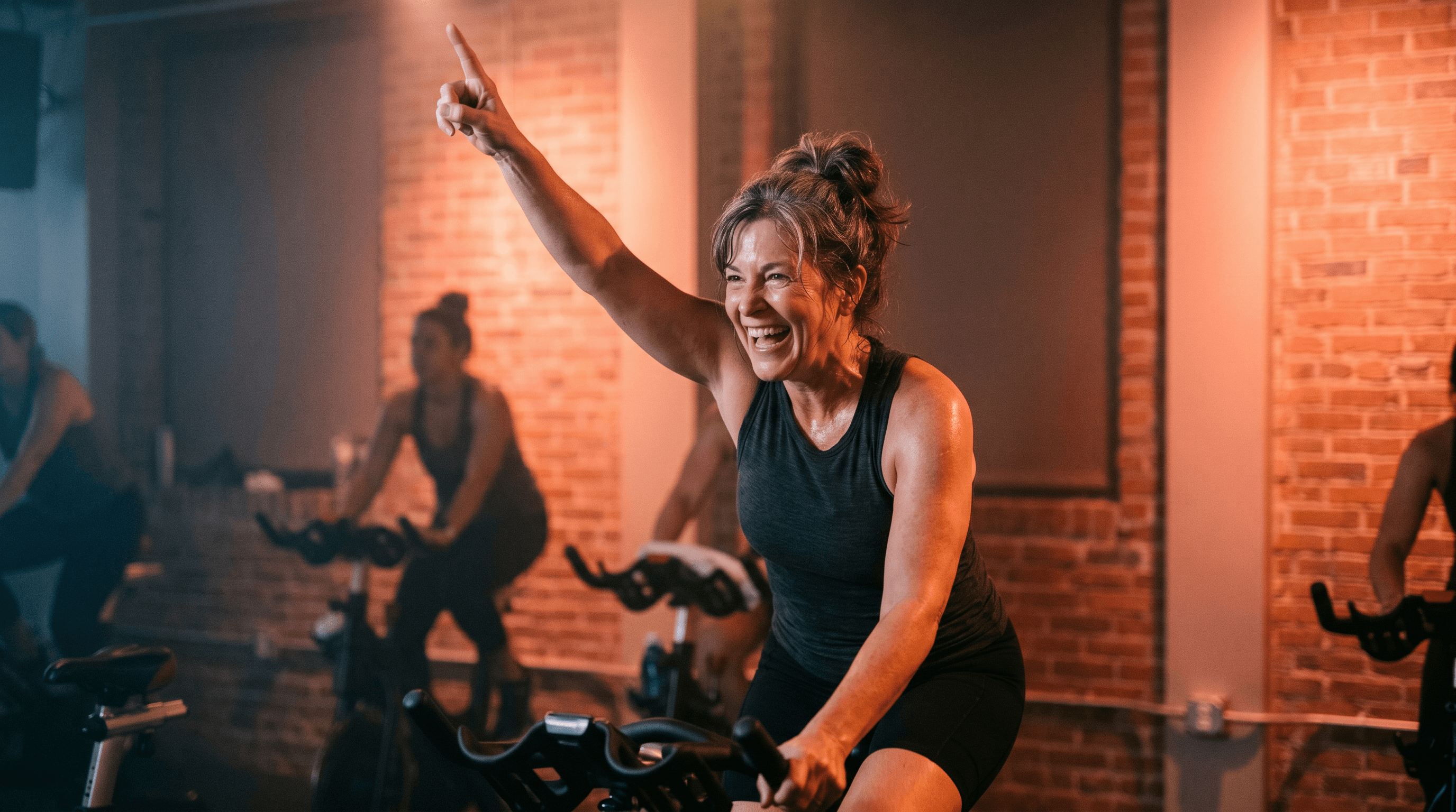 A FortCycle rider mid-class with arm raised under coral lighting